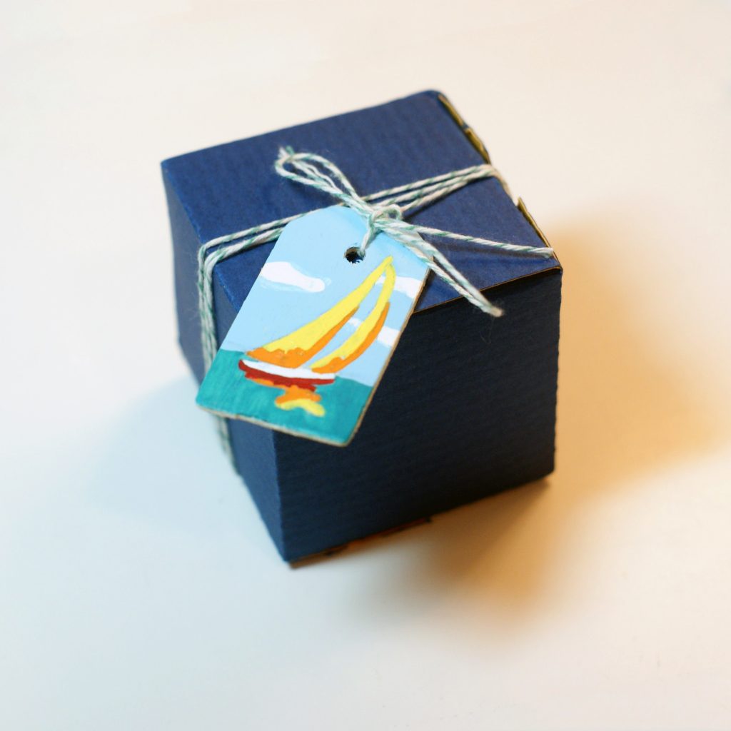 bright sailboat painted on wood tag and hung on a square package